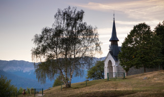 Paisaje al atardecer cerca de Divonne Les Bains, con capilla, árboles y montañas en Auvergne-Rhône-Alpes, Francia.
