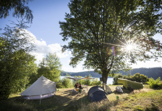 Zonnig kampeerterrein met tenten aan het meer bij Huttopia Lac de la Siauve, Auvergne-Rhône-Alpes, Frankrijk.