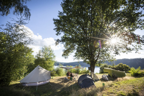 Sunny campsite with tents by the lake at Huttopia Lac de la Siauve, Auvergne-Rhône-Alpes, France.