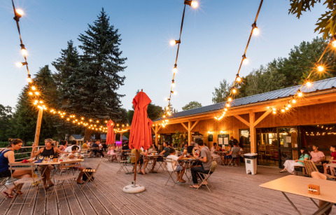 Personas cenando al aire libre bajo luces en Huttopia Lac de la Siauve, parque vacacional en Francia.