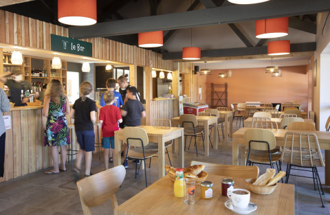 Cafetería en Huttopia Lac de la Siauve con personas en el mostrador y desayuno servido en las mesas.