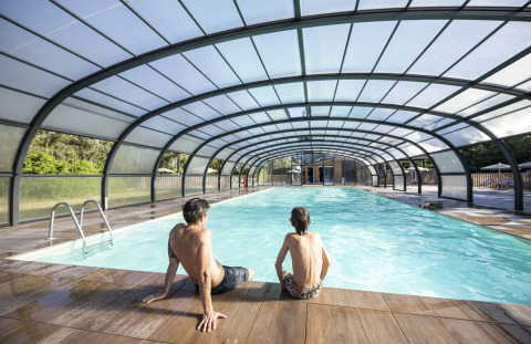 Dos personas se sientan junto a una piscina cubierta en Huttopia Lac de la Siauve, Auvergne-Rhône-Alpes, Francia.