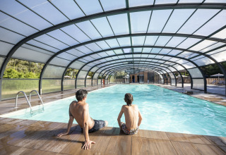 Two people sit by an indoor pool at Huttopia Lac de la Siauve holiday park, Auvergne-Rhône-Alpes, France.