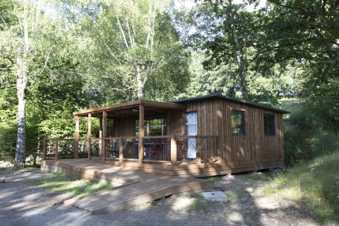 Cabaña de madera con terraza cubierta entre árboles, en Huttopia Lac de la Siauve, Auvergne-Rhône-Alpes, Francia.