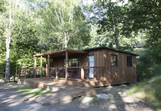 Casetta in legno con veranda coperta circondata da alberi a Huttopia Lac de la Siauve, Auvergne-Rhône-Alpes, Francia.