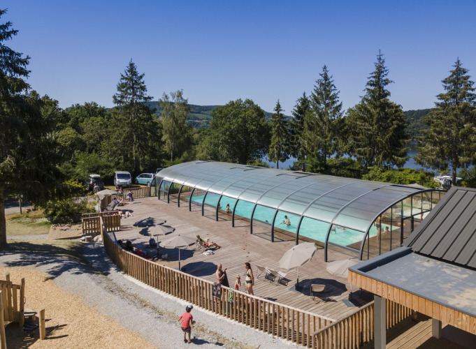 Outdoor pool with glass enclosure and sun deck at Huttopia Lac de la Siauve holiday park in Auvergne-Rhône-Alpes, France.