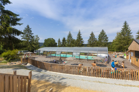 Udendørs swimmingpool med overdækning og folk, der nyder solen i en feriepark i Auvergne-Rhône-Alpes, Frankrig.