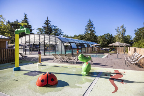 Zona de piscina al aire libre con tumbonas, figuras de juego y piscina cubierta en Huttopia Lac de la Siauve, Francia.