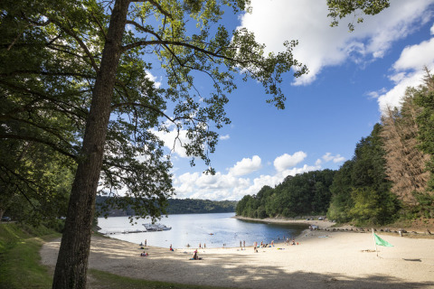 Playa arenosa con visitantes en Huttopia Lac de la Siauve, parque vacacional en Auvergne-Rhône-Alpes, Francia.