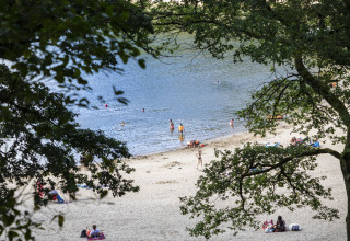 Zicht op het strand van Huttopia Lac de la Siauve, waar gezinnen relaxen en zwemmen in het meer.