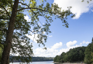Zandstrand met mensen, kalm meer en groene bomen bij Huttopia Lac de la Siauve, Auvergne-Rhône-Alpes.