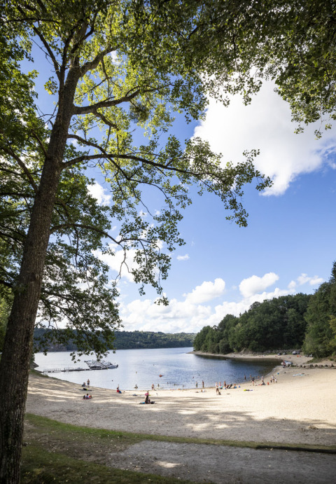 Vista de una playa arenosa con personas, lago tranquilo y árboles verdes en Huttopia Lac de la Siauve, Auvernia-Ródano-Alpes.