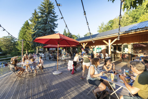 Personas disfrutan de una comida al aire libre en la terraza soleada de Huttopia Lac de la Siauve, en Francia.
