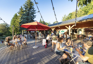 Mensen genieten van eten en drank op het zonovergoten terras van Huttopia Lac de la Siauve, Frankrijk.
