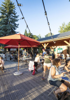 Personas disfrutan de una comida al aire libre en la terraza soleada de Huttopia Lac de la Siauve, en Francia.