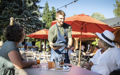 Waiter serving two women at an outdoor café at Huttopia Lac de la Siauve holiday park in France.