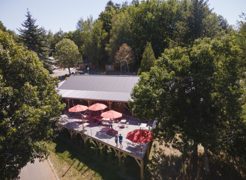 Terras met rode parasols omringd door bomen in vakantiepark Huttopia Lac de la Siauve, Frankrijk.