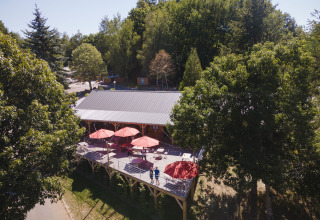 A scenic terrace with red umbrellas at Huttopia Lac de la Siauve holiday park nestled among trees in France.