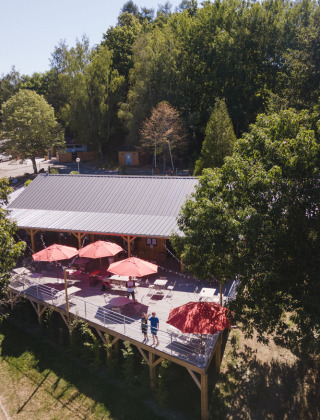 Vista de una terraza con sombrillas rojas entre árboles en Huttopia Lac de la Siauve, un parque en Francia.