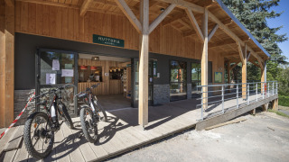 Entrada de Huttopia Lac de la Siauve con porche de madera, bicicletas de alquiler y recepción en Auvergne-Rhône-Alpes.
