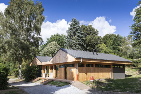 Bâtiment moderne en bois entouré de verdure au Huttopia Lac de la Siauve, en Auvergne-Rhône-Alpes, France.