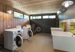 Laundry room with washing machines and large sinks at Huttopia Lac de la Siauve, holiday park in Auvergne-Rhône-Alpes, France.