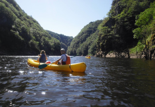 Twee personen varen in een gele kajak op een rivier omringd door groene heuvels bij Lanobre, Frankrijk.