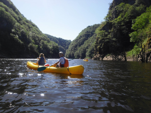 Two people in a yellow kayak paddle along a river surrounded by green hills near Lanobre, France.