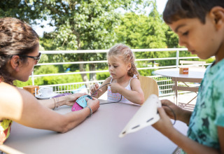 Enfants et adulte faisant des activités manuelles à une table à Huttopia Lac de la Siauve, Auvergne-Rhône-Alpes.