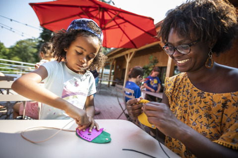 A child and a woman doing crafts together at a table in Huttopia Lac de la Siauve holiday park, France.