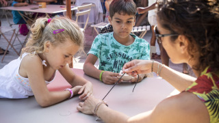 Niños participan en una actividad manual con un adulto en Huttopia Lac de la Siauve, parque vacacional en Francia.
