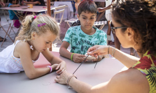Niños participan en una actividad manual con un adulto en Huttopia Lac de la Siauve, parque vacacional en Francia.