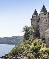 Castillo medieval junto al lago cerca de Lanobre, Auvergne-Rhône-Alpes, Francia, rodeado de naturaleza verde.