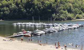 Personas nadan y disfrutan en una playa de Lanobre, Francia, con botes atracados en el muelle cercano.