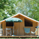 Safari-teltet Toile&bois Classic med stole, bord og parasol på trædæk, omgivet af grønne træer.