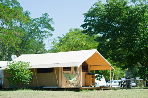 Tienda de safari Toile&bois clásica en Huttopia le Moulin, Francia, rodeada de árboles y naturaleza verde.