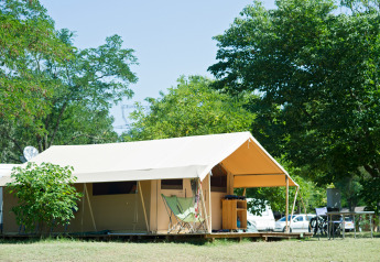 Tienda de safari Toile&bois clásica en Huttopia le Moulin, Francia, rodeada de árboles y naturaleza verde.