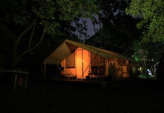 Tienda safari Toile&bois Classic iluminada en Huttopia le Moulin, Francia, rodeada de árboles de noche.