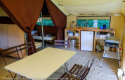 Interior of a safari tent with kitchen, dining table, and beds at Huttopia le Moulin, France.