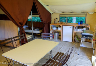 Interior de una tienda safari con cocina, mesa de comedor y camas en Huttopia le Moulin, Francia.