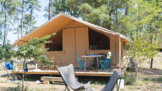 Tenda safari Toile&bois Classic in campeggio forestale, con terrazza in legno e area salotto all'aperto.