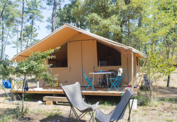 Tente safari Toile&bois Classic sur un camping en forêt, avec terrasse en bois et coin salon extérieur.
