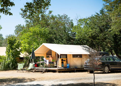 Safari-Zelt Toile&bois Classic im Huttopia le Moulin in Frankreich, umgeben von Bäumen und Campingausrüstung.