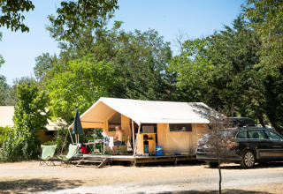 Tente safari Toile&bois Classic à Huttopia le Moulin, France, avec arbres, chaises extérieures et voiture.