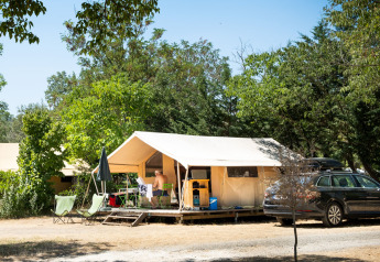 Safari-Zelt Toile&bois Classic im Huttopia le Moulin in Frankreich, umgeben von Bäumen und Campingausrüstung.