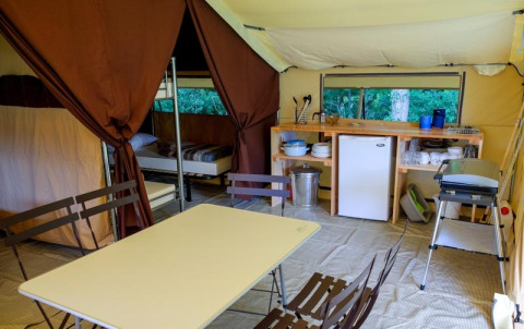 Inside view of a Toile&bois Classic safari tent at Huttopia le Moulin, with kitchen, beds, and table.
