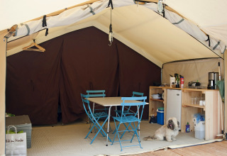 Binnenkant van een safaritent met eettafel, keukentje en een hond op de grond bij Huttopia le Moulin, Frankrijk.