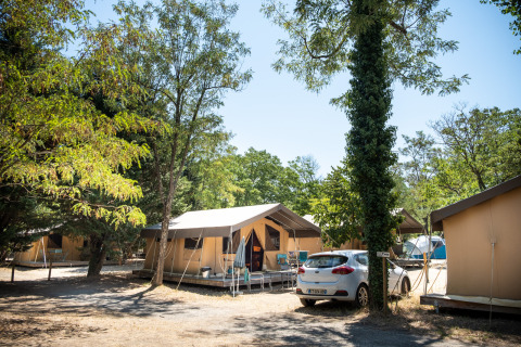 Safaritent op camping, Toile&Bois tent Sweet, omringd door bomen en geparkeerde auto, zomerse sfeer.