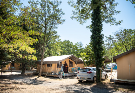 Tienda safari en un camping, Toile&Bois tent Sweet, rodeado de árboles y un coche aparcado al costado.