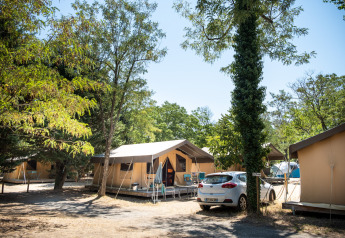 Tienda safari en un camping, Toile&Bois tent Sweet, rodeado de árboles y un coche aparcado al costado.